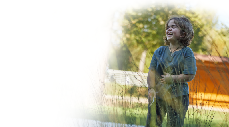 Ein junges Mädchen mit Achondroplasie, das lachend eine Kristallhalskette trägt.