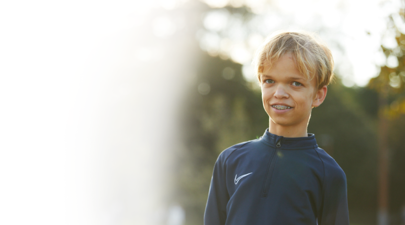 Ein blondhaariger Junge mit Achondroplasie, der eine Zahnspange und ein Laufshirt trägt.