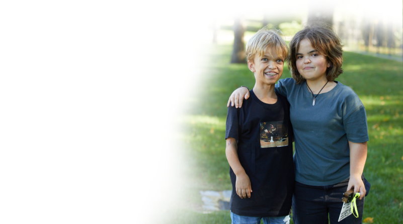 Ein Junge und ein Mädchen mit Achondroplasie stehen zusammen und legen jeweils einen Arm umeinander.