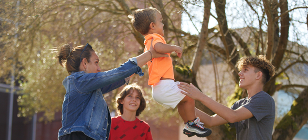 a woman holds up a young boy with achondroplasia and passes him to her teenage son