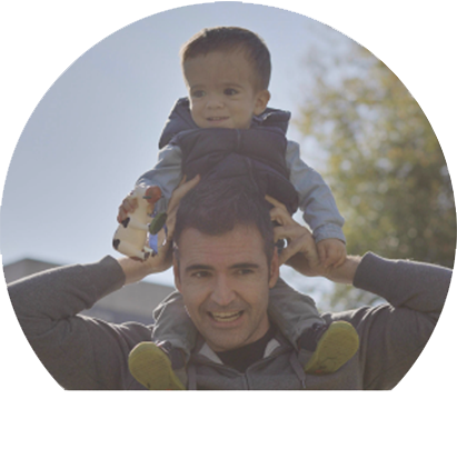 a young boy with Achondroplasia holds a toy while sitting on a mans shoulders