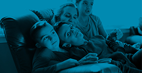 a boy with Achondroplasia sits on the couch with his siblings and mother