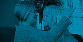 a girl with Dwarfism smiling and grabbing her mother's finger