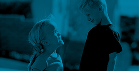 A young girl with Achondroplasia looks up at her brother outside