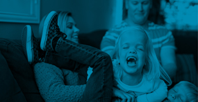 a girl with skeletal dysplasia laughing with her mom, dad and brother on the couch